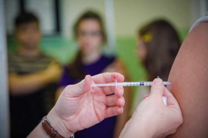 Nurse,Administering,Vaccination,To,Students,Arms,In,A,High,School.