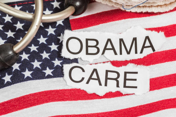 Obama,Care,In,Torn,Paper,On,American,Flag,With,Stethoscope