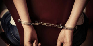 Hands handcuffed behind a chair, viewed from the back