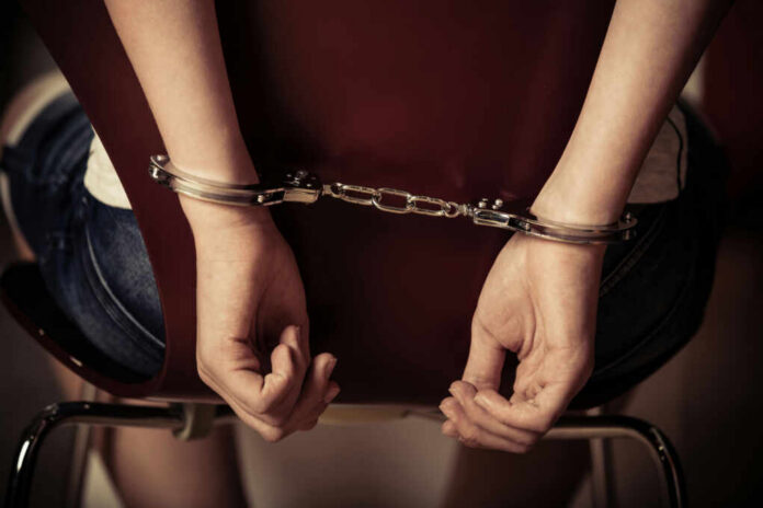 Hands handcuffed behind a chair, viewed from the back