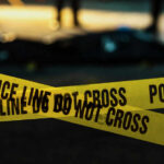 Yellow police caution tape at a crime scene with blurred figures in the background