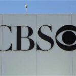 CBS logo displayed on a white wall with a blue sky background