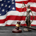 A gavel and a statue of Lady Justice in front of an American flag