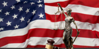 A gavel and a statue of Lady Justice in front of an American flag
