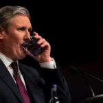 Man in formal attire drinking water during a speech