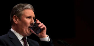 Man in formal attire drinking water during a speech