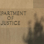 Sign reading Department of Justice on a stone wall with a shadow