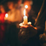 People holding lit candles in a dimly lit setting