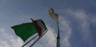 Two flags on a flagpole against a blue sky with clouds