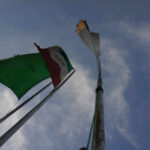 Two flags on a flagpole against a blue sky with clouds