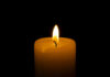 A lit candle with a soft flame against a black background