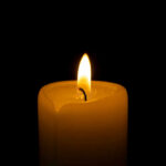 A lit candle with a soft flame against a black background