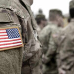 Close-up of a soldiers uniform with an American flag patch, surrounded by other soldiers