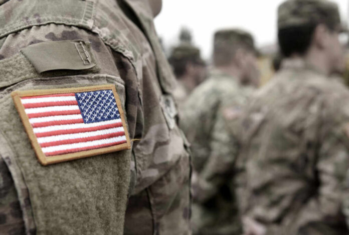 Close-up of a soldiers uniform with an American flag patch, surrounded by other soldiers