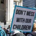 A protester holding a sign that reads 'DON'T MESS WITH OUR CHILDREN'