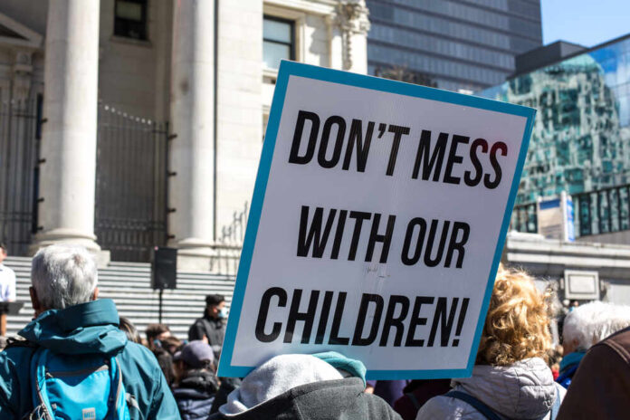 shutterstock_1953475393.jpg A protester holding a sign that reads 'DON'T MESS WITH OUR CHILDREN'
