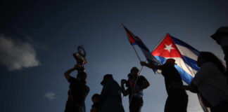 Silhouetted figures celebrating with a trophy and Cuban flags against a sunset sky