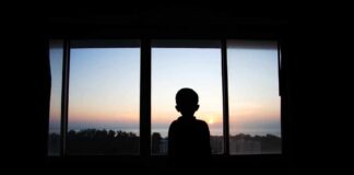 Silhouette of a child looking out a window at a sunset
