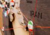 Close-up of a wooden map highlighting Iran with travel pins and red strings
