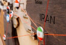 Close-up of a wooden map highlighting Iran with travel pins and red strings