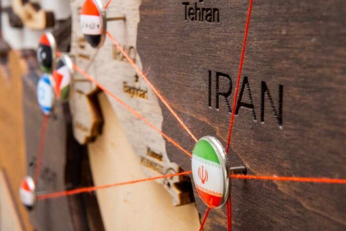 shutterstock_2254527291.jpg Close-up of a wooden map highlighting Iran with travel pins and red strings