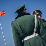 Two Chinese soldiers in military uniforms with a flag in the background
