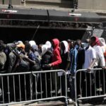 A crowd of people waiting in line outside a venue with a security officer present