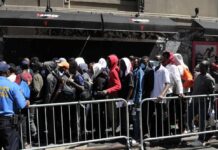 A crowd of people waiting in line outside a venue with a security officer present