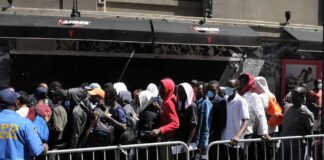 Reparations for Illegal Immigrants: Radical Proposal Unveiled A crowd of people waiting in line outside a venue with a security officer present