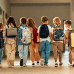 A group of children walking together in a school hallway, each carrying a backpack