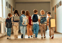 A group of children walking together in a school hallway, each carrying a backpack