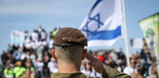 Soldier saluting in front of a crowd with the Israeli flag in the background