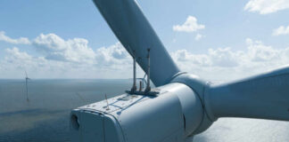 Close-up view of a wind turbine with a blue sky and ocean in the background