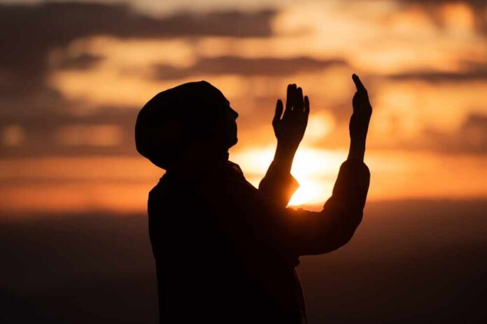 shutterstock_2593754351.jpg Silhouette of a person with raised hands against a sunset