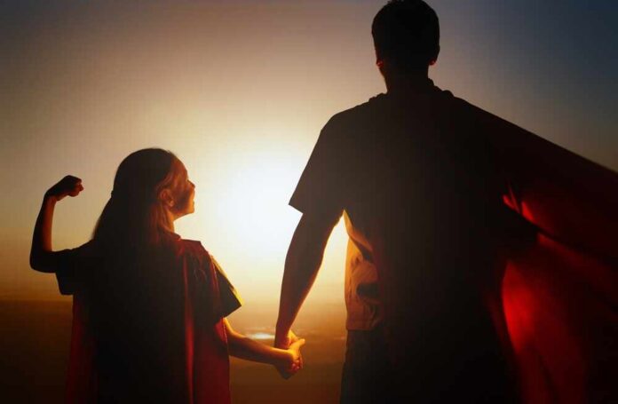 Silhouette of a parent and child wearing capes against a sunset