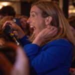A woman in a blue jacket expressing excitement in a crowded event