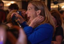 A woman in a blue jacket expressing excitement in a crowded event