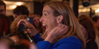 A woman in a blue jacket expressing excitement in a crowded event