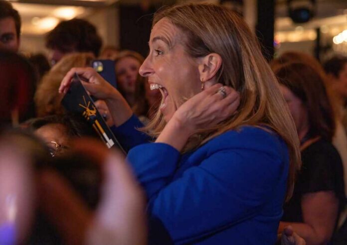 A woman in a blue jacket expressing excitement in a crowded event