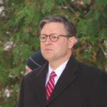 Man in formal attire with glasses standing outdoors