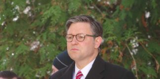 Man in formal attire with glasses standing outdoors