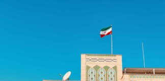 Building with intricate patterns and the Iranian flag against a clear blue sky