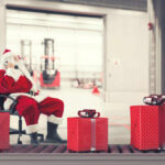 Santa Claus sitting in a chair making a phone call with Christmas gifts nearby