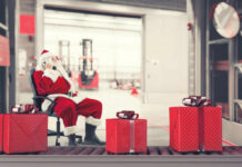 Santa Claus sitting in a chair making a phone call with Christmas gifts nearby