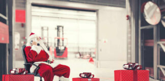 Santa Claus sitting in a chair making a phone call with Christmas gifts nearby