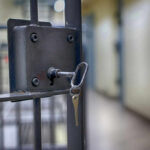 Close-up of a locked jail cell door with a key inserted