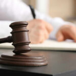 Court’s Stunning Ruling Halts VA Redistricting Plan A gavel on a desk with a blurred hand writing in the background