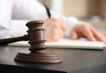 A gavel on a desk with a blurred hand writing in the background