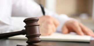 A gavel on a desk with a blurred hand writing in the background