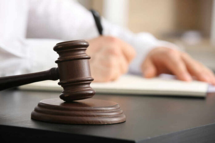 A gavel on a desk with a blurred hand writing in the background